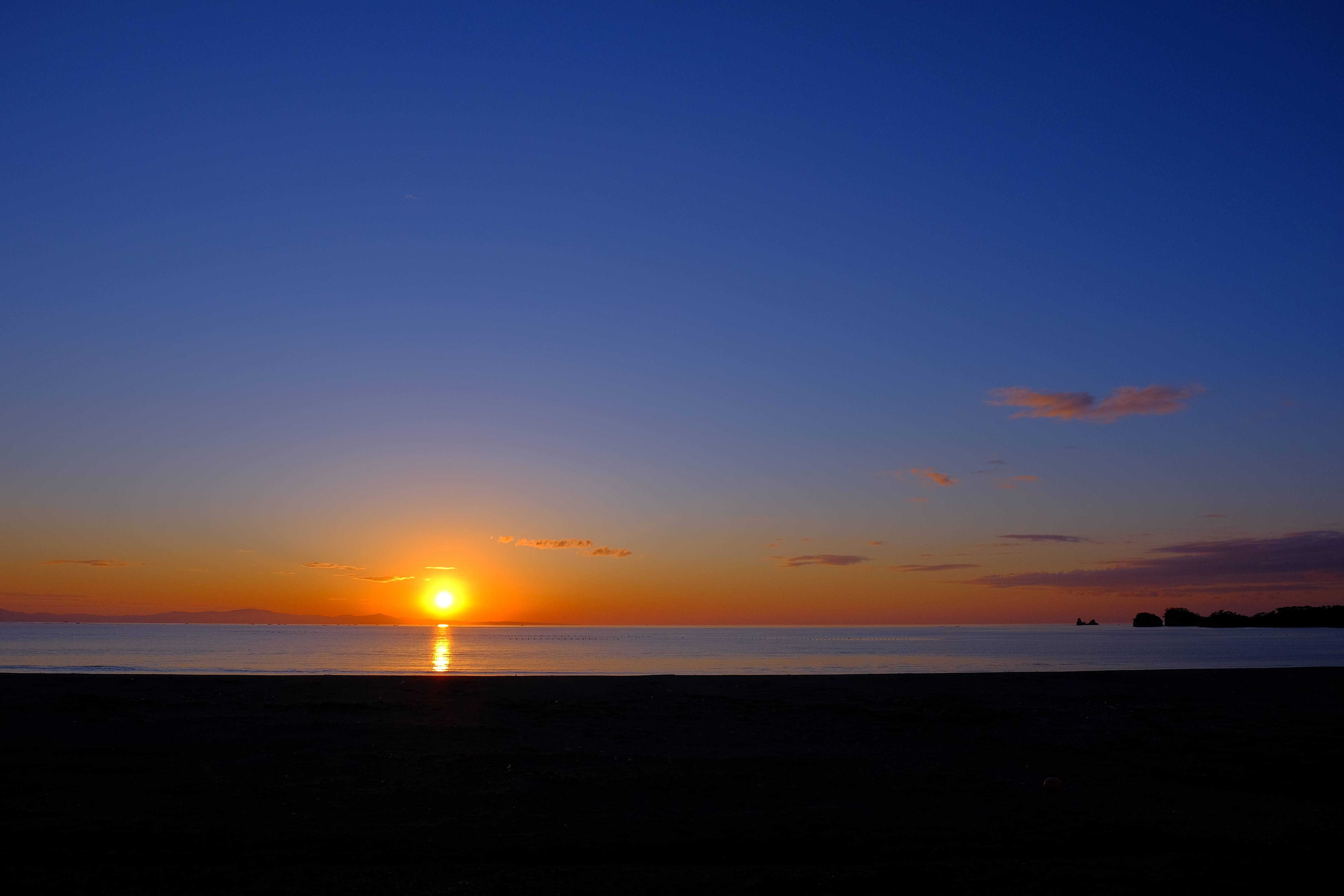 海辺から見た美しい夕日。青いグラデーションの空とオレンジ色の水平線が印象的な風景写真