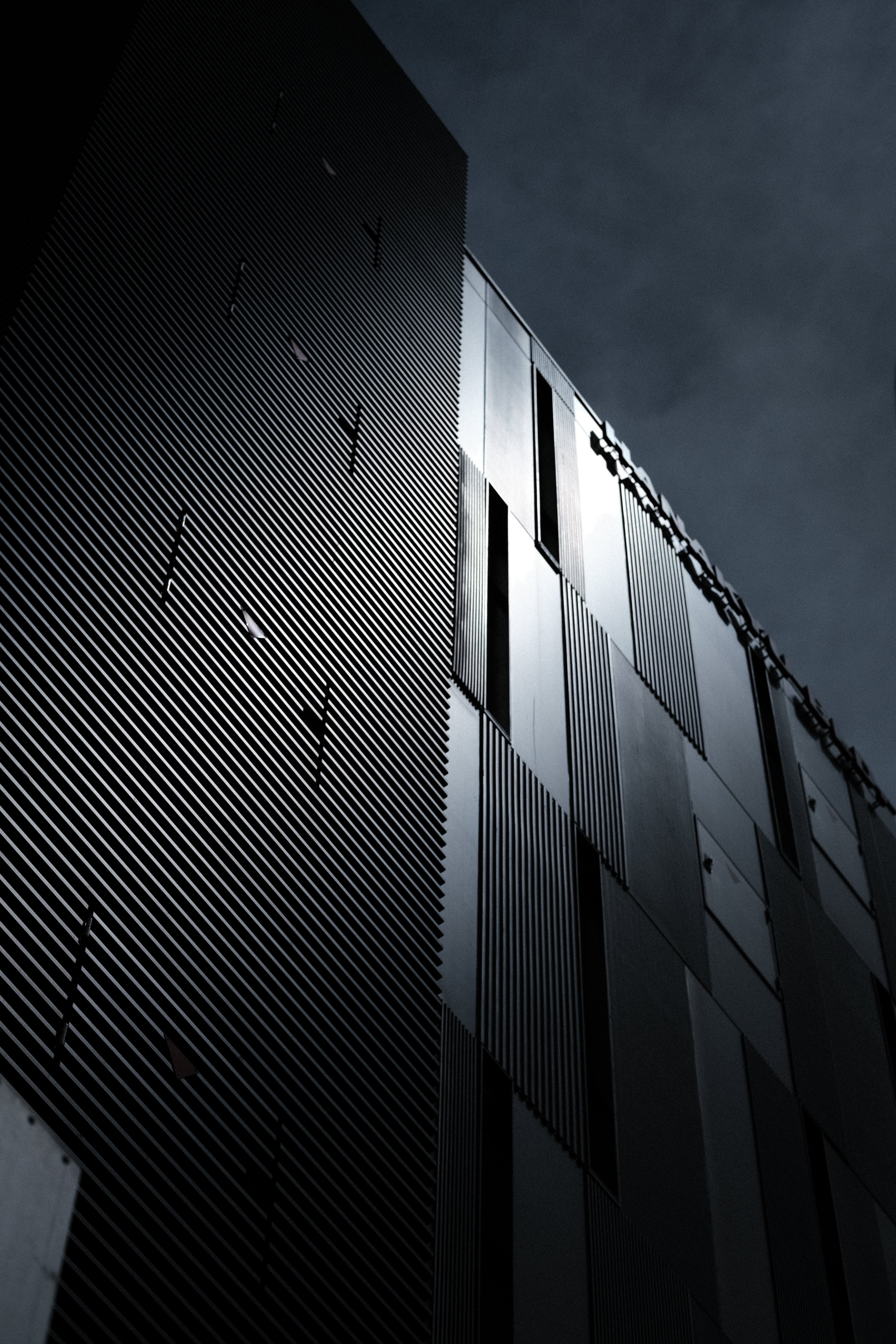 近代建築の外壁を斜め下から撮影。金属の格子状のパネルが幾何学的なパターンを描くモノトーンの抽象写真