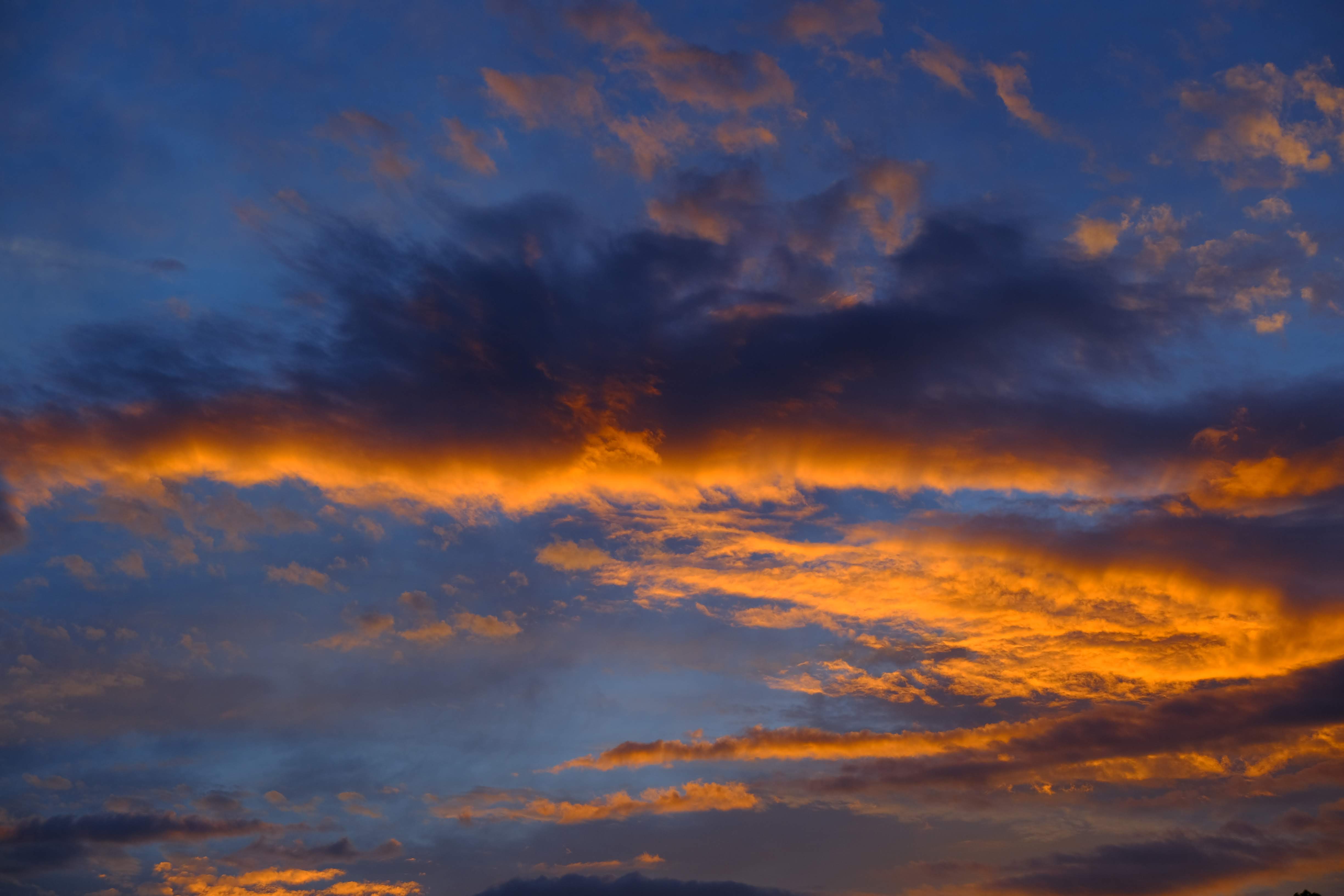 夕暮れの劇的な空。オレンジ色の光に縁取られた雲が青い空に広がり、ドラマチックな夕焼けを演出
